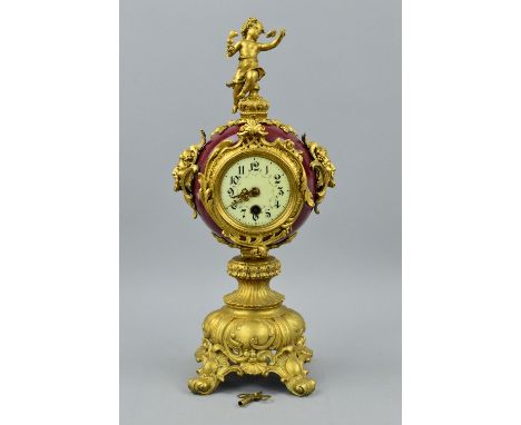 A LATE 19TH/EARLY 20TH CENTURY GILT METAL AND PORCELAIN MANTEL CLOCK, figural surmount on circular claret glazed case with Ba