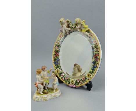 A LATE 19TH/EARLY 20TH CENTURY CONTINENTAL PORCELAIN OVAL WALL MIRROR, the frame modelled with two cherubs holding a floral s