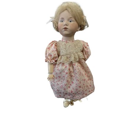 A bisque head Kammer and Reinhardt doll, in pink floral dress. With painted blue eyes and blonde hair, marked to rear of head