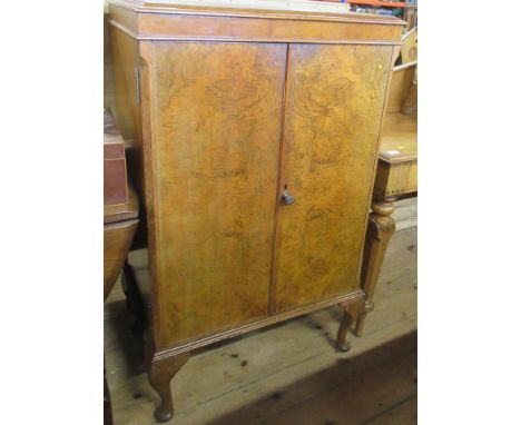 A Wilson &amp; Gill London walnut veneered drinks cabinet, with hinged rising lid, over a pair of doors revealing drawers and