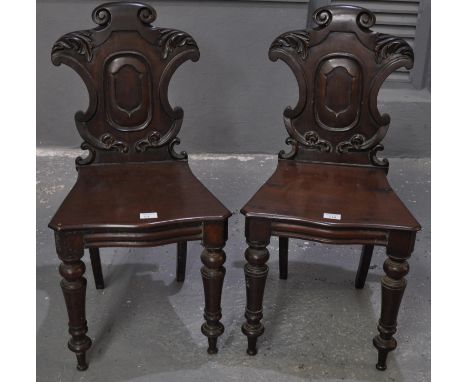 A pair of Victorian mahogany hall chairs with carved foliate and moulded backs, above a serpentine moulded seat standing on r