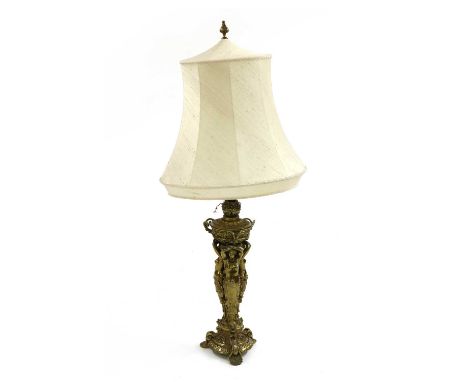A large late Victorian gilt metal lamp, designed as three maidens holding a container on scroll scallop shell feet, a convert