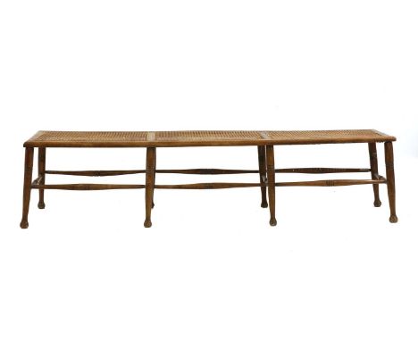 A beech and wicker topped long stool, the top carved in three panels and raised on eight ring turned legs united by stretcher