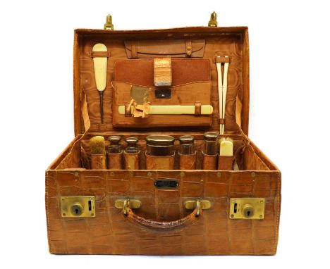 An Edwardian crocodile leather vanity case, labelled 'Drew &amp; Co', fitted five silver topped glass dressing jars, ivory ba