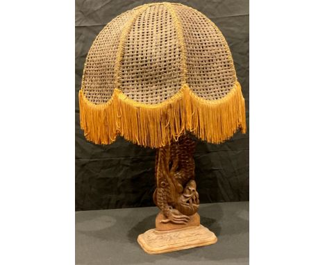 An Indonesian style carved openwork table lamp as a dragon, fringed wicker work shade, 57cm overall 