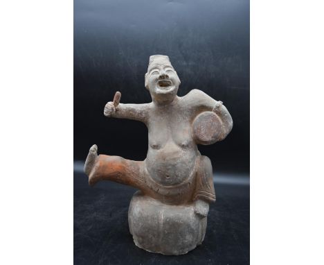 A Han or later Chinese terracotta glazed theatrical figure, perched on a stone and playing the drum. H.40 W.29cm 