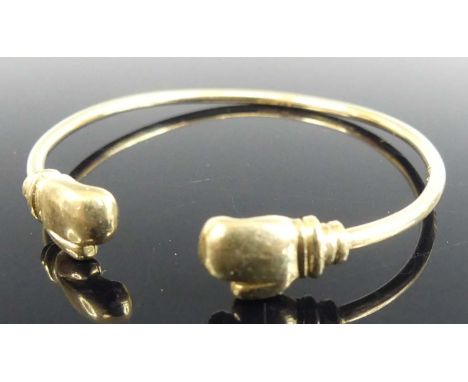 A child's 9ct gold bangle, the ends each set with a boxing glove, dia.5cm, 7.9g