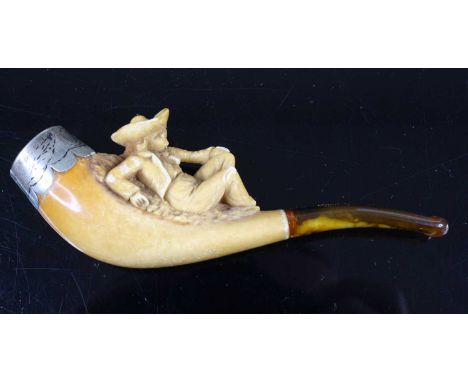 A 19th century meerschaum pipe, the bowl carved as a reclining figure in hat and cape, having a faux amber mouthpiece and eng