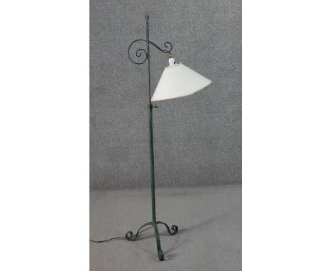 A Victorian style wrought iron standard lamp with a verdigris finish, a cream coloured shade, on tripod feet with scroll ends