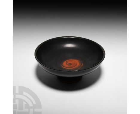 Circa 5th century B.C. A black-glazed kylix or stemmed cup created without handles, composed of a D-section bowl with attract