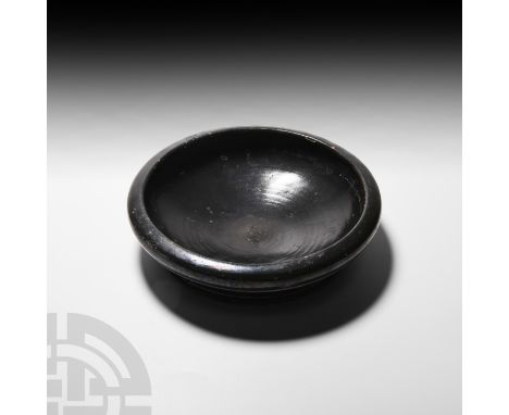 5th-3rd century B.C. A black-glazed plate or shallow bowl with D-section rim and everted foot, pierced twice for suspension, 