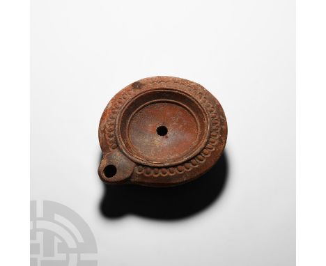 Late 2nd century A.D. A terracotta oil lamp composed of a circular discus with tapering sidewall, D-shaped nozzle with sub-ci