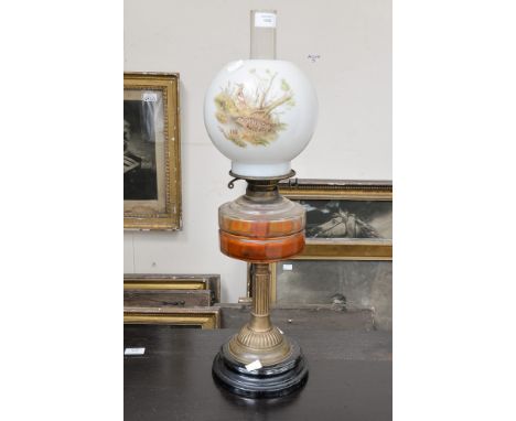 A Victorian oil lamp, having ebonized base, brass pedestal, amber glass reservoir and shade decorated with woodcock