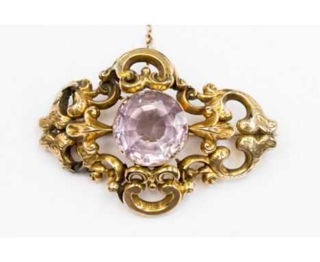 A Victorian yellow metal and amethyst brooch, with an ornate open scroll design, with engraved floral motifs. The brooch is s