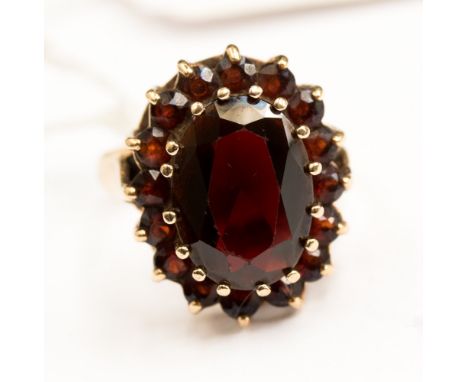 A 9ct gold ring with large oval garnet to the centre with smaller round garnet surround, size N1/2 with a total gross weight 