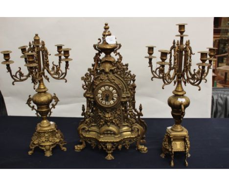 A cast brass German mantle clock and garniture, the clock having individual set enamelled Roman numerals to the dial with key
