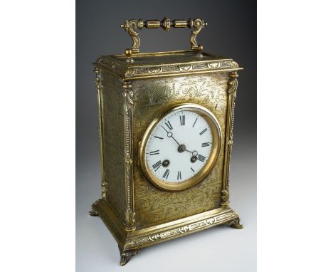 A Victorian brass mantle clock white enamel dial with Roman numerals, with carrying handle, ornate borders on scroll feet, th