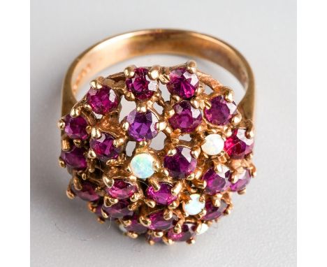 A 1970s 9ct gold ruby and opal dress ring. Deigned as an oval shape dome set throughout with rubies and opal cabochons, to th