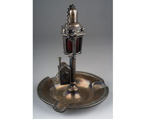 An early 20th Century American white metal combination ashtray, cutter and lighter in the form of a lamp with ruby glass rese