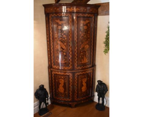 An early 19th century Dutch marquetry inlaid freestanding bowfronted corner cupboard, the moulded cornice above twin upper cu