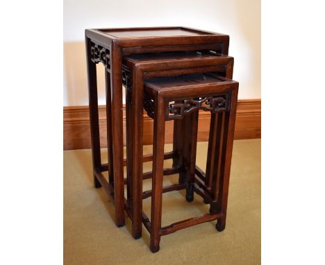 A Chinese nest of three hardwood occasional tables with pierced friezes, raised on square sectioned supports united by stretc