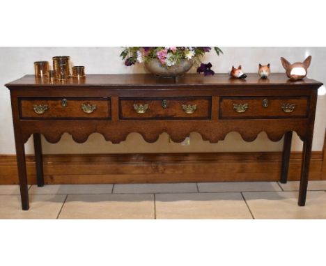 A George III North Country oak and mahogany crossbanded dresser base, the plank top above three drawers with brass drop handl