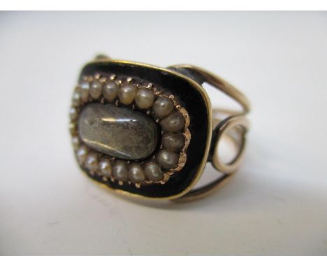 A Victorian yellow metal mourning ring with woven hair behind a glass panel within a black enamelled and seed pearl setting, 