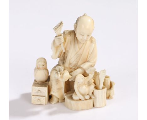 Japanese Meiji period ivory Okimono, carved as a daruma toy maker with tools and drawers surrounding, black lacquer signed pl