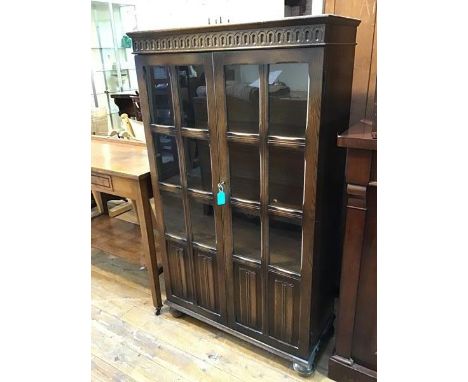 A 1920s/30s oak bookcase, the cornice with moulded frieze above a pair of doors, each with six glass panes above two linenfol