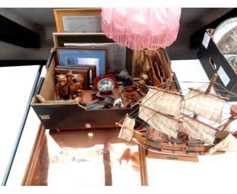 A box containing  brass table lamp with shade, wooden animal ornaments, wooden model of a galleon, framed pictures, etched co