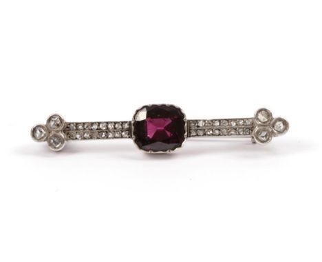 A Garnet and Diamond Brooch, the cushion cut garnet in a crimped setting centres two parallel rows of rose cut diamonds to tr