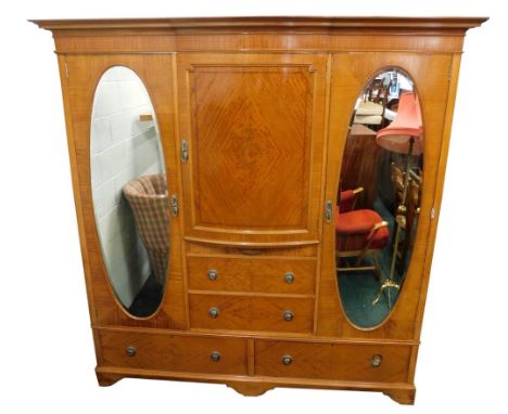 An Edwardian light mahogany and inlaid triple wardrobe, with moulded cornice raised above a curved front cupboard above two d