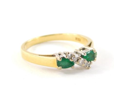 An 18ct gold emerald and diamond dress ring, set with two pear cut emeralds, each stone approximately 0.20cts, in a white fou