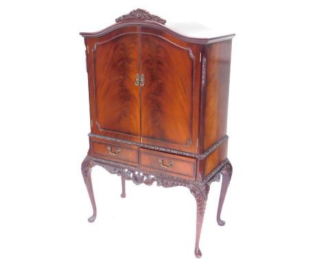 A figured mahogany cocktail cabinet, the arched top with a carved crest above two doors enclosing a maple veneered interior w