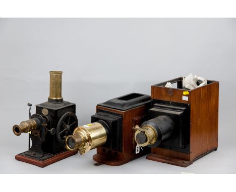 A vintage tinplate and brass Magic Lantern film projector with white pottery winder on wooden base and two mahogany tin and b