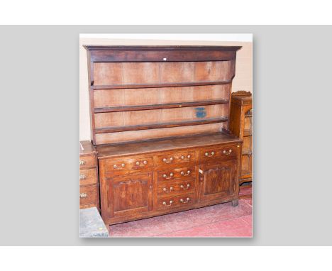 A Georgian oak dresser with closed back three shelf plate rack in pine, the two plank top over an arrangement of two drawers 