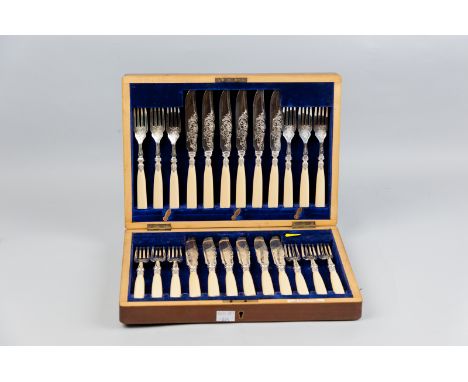 A mahogany cased set of twelve fish knives and forks, all having bright cut decorated blades, leaf pattern ferrules and ivory