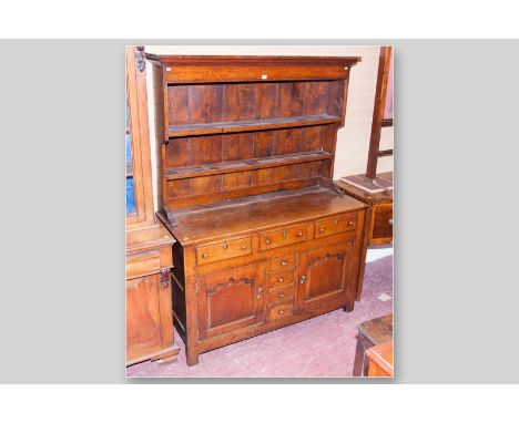 An oak Caernarfonshire dresser having a simple two shelf rack with shaped crown above a two plank base with an arrangement of