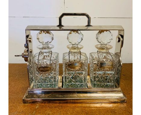 A White Metal Tantalus with key and hallmarked silver decanter labels.(Two Brandy and a Whisky)