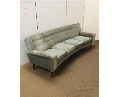 A mid century curved button back four seater sofa on a six tapered legs upholstered in a pale green velvet 