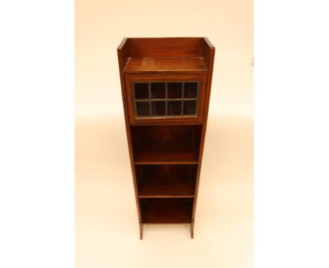 An early 20th Century mahogany and boxwood strung narrow book shelf, the upper shelf enclosed by a small leaded glazed panell