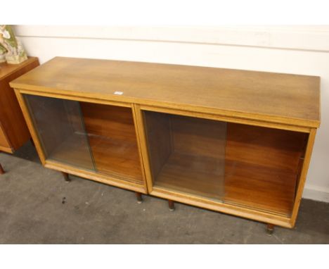 A 1960's light oak bookcase, the interior adjustable shelves enclosed by two pairs of glazed sliding doors raised on rounded 