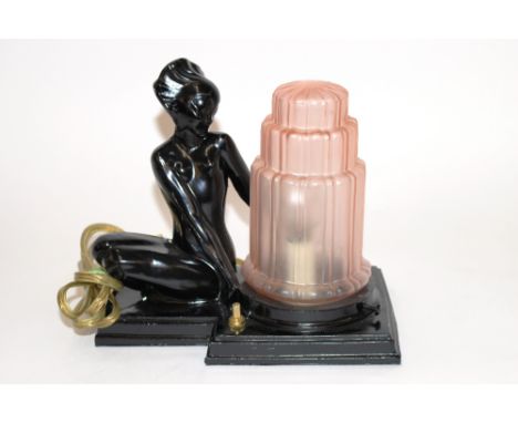 An Art Deco table lamp in the form of a stylised seated nude beside a pink glass stepped shade, 23cm long x 20cm high