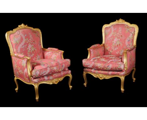 A pair of French giltwood bergeres armchairs in Louis XV style, each with a padded back and seat, the moulded frame carved wi