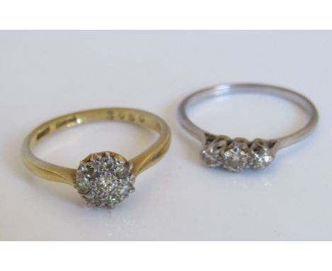 Two diamond rings; the first of flower head form in 18ct gold and the second a platinum three stone example, sizes M & K, 4g 