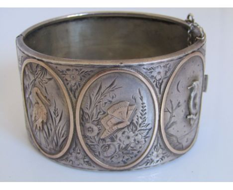 A Victorian sterling silver hinged cuff bangle engraved with three panels depicting a crane, butterfly and woodpecker in natu