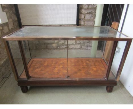 An early 20th century shop counter with plate glass panels, within a brass frame work, the lower shelf with parquetry detail,