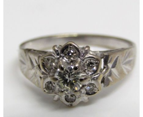 A diamond flower head ring in unmarked white metal with bright cut decoration to the shoulders, central diamond 0.25 cts appr