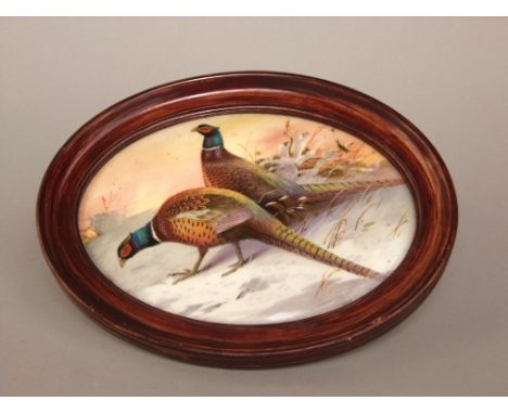 An oval ceramic plaque with painted decoration of a pair of pheasants in the snow, signed bottom right JC Dean? 17cm max in o