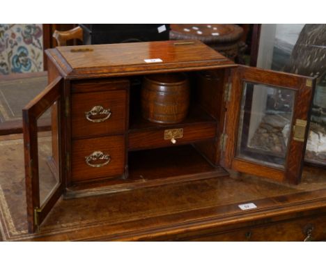 A Victorian oak smoker's compendium, a pair of bevelled glazed doors open to reveal two drawers flanked by a shelf with tobac